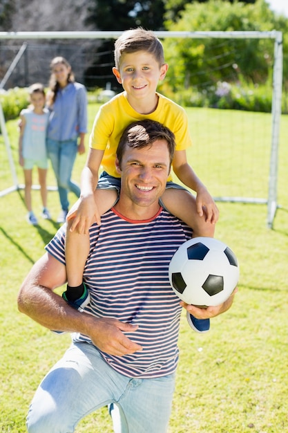 Pai sorridente com futebol carregando o filho no ombro no parque