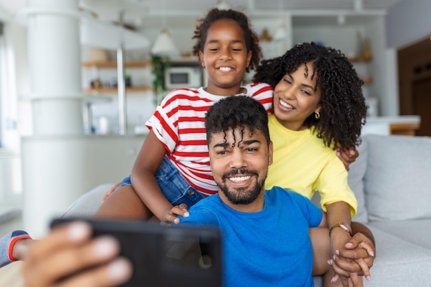 Pai sorridente segurando o celular fazendo selfie gravando vídeo com esposa e filha felizes Pais animados olhando para a tela do celular com criança se sentindo animada