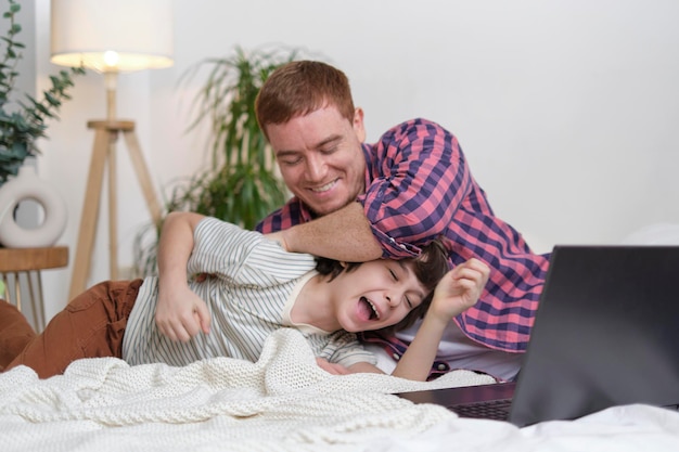 Pai tentando relaxar com laptop e séries de TV, mas filho alegre o envolve em uma distração mais divertida