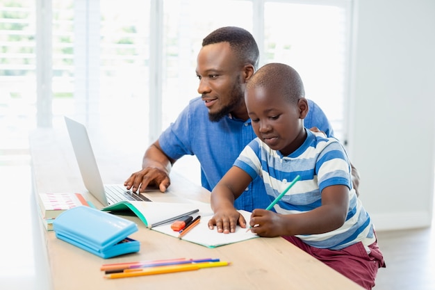 Pai usando laptop e filho fazendo sua lição de casa na sala de estar