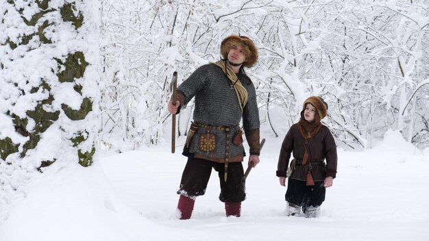 Pai viking com filho na floresta de inverno pai conversando com filho segurando machado nas mãos