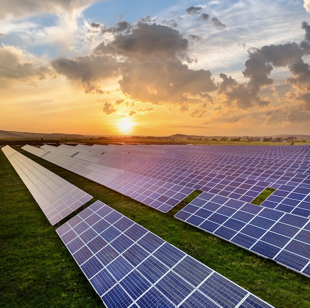 Foto painéis solares solares azuis produzindo energia limpa renovável na paisagem rural e fundo de sol poente.