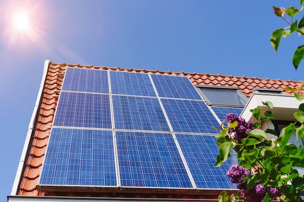 Painel solar em um telhado vermelho refletindo o sol e o céu azul sem nuvens