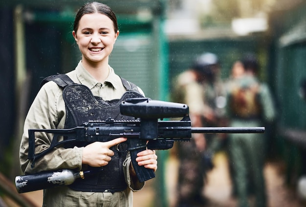 Paintball glücklich und Porträt einer Frau mit Waffe in Sicherheitsuniform für Outdoor-Schießspiel mit Lächeln Aufgeregtes Turniermädchen im Westenschutz bereit für Shooter-Sport und Aktivität