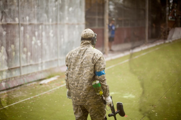 Paintball-Sportspieler in Schutzuniform und Maske, die im Freien mit der Waffe spielen