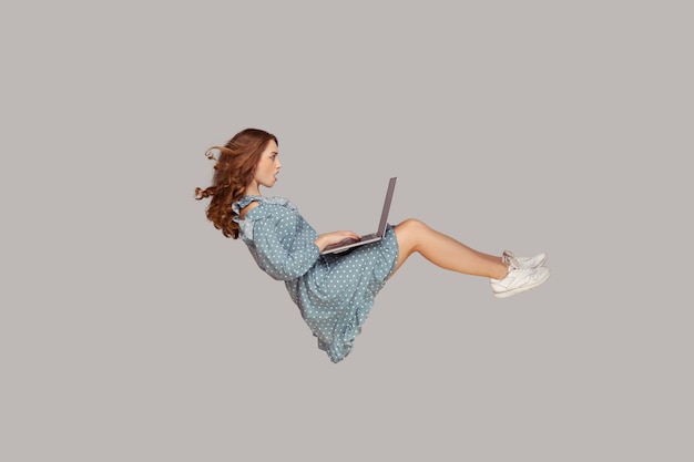 Pairando no ar. Menina surpresa com babado vestido levitando, olhando para a tela do laptop chocada e maravilhada