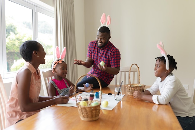 Foto pais africanos-americanos felizes com filho e filha usando orelhas de coelho pintando ovos de páscoa