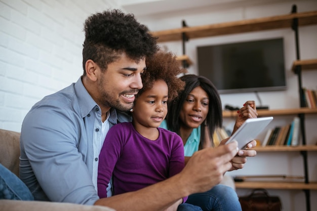 Pais afro-americanos ensinando sua filha a usar tablet digital em casa