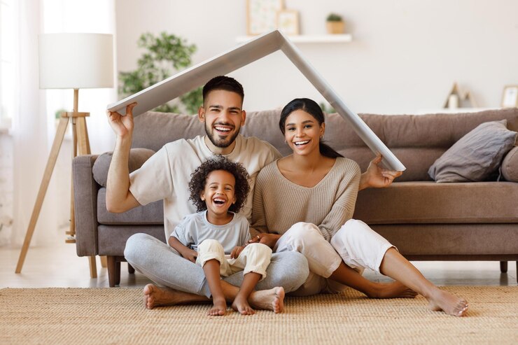Foto pais alegres com criança sorrindo e mantendo a maquete do telhado sobre as cabeças enquanto está sentado no chão na sala de estar aconchegante durante a realocação