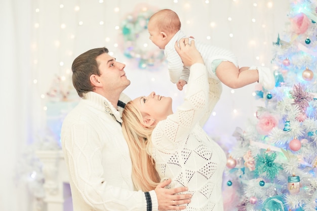 Pais amorosos brincando com seu bebê em pé na festiva sala de estar. o conceito de natal