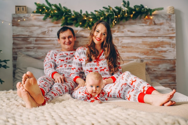 Pais com sua filha pequena em roupas de férias com veados impressos e flocos de neve sentado na cama