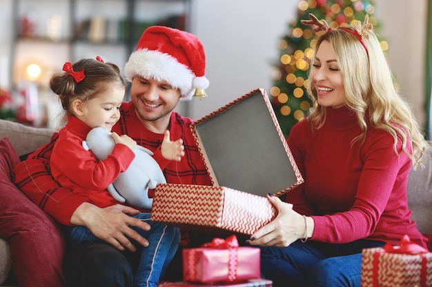 Pais de família felizes e filha abrem presentes na manhã de Natal