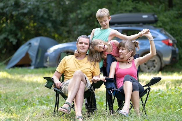 Pais de família jovens felizes e seus filhos descansando juntos no local de acampamento no verão.