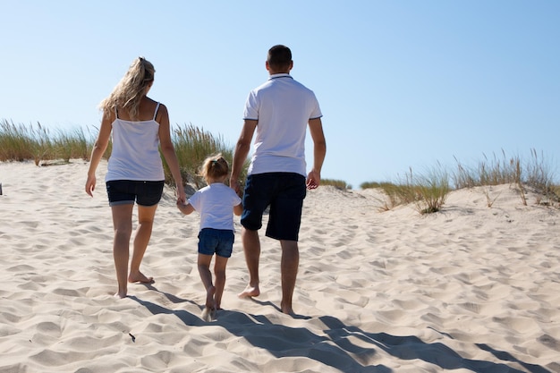 Pais de mãos dadas filha filha e andando na praia de dunas de areia em férias