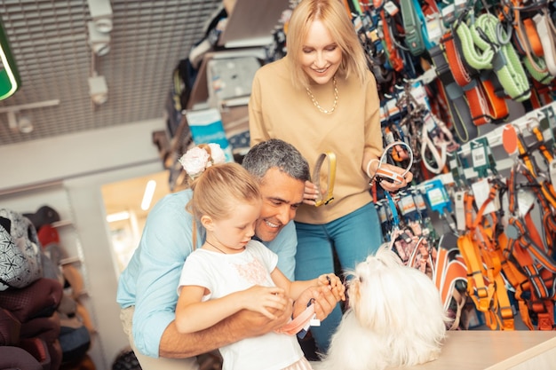 Foto pais e filha escolhendo coleira de cachorro para seu cachorro fofo branco