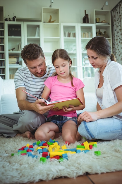 Foto pais e filha lendo um livro enquanto brincava com blocos de construção