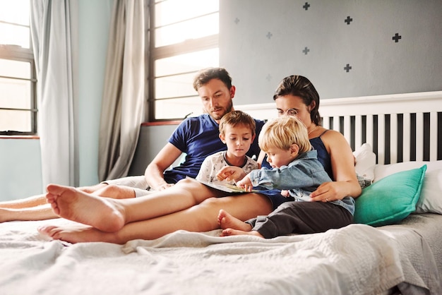 Pais e filhos sentados na cama em casa.