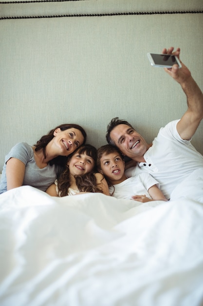 Foto pais e filhos tomando uma selfie na cama