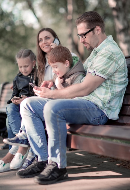 Foto pais e filhos usando seus smartphones sentados em um banco de parque