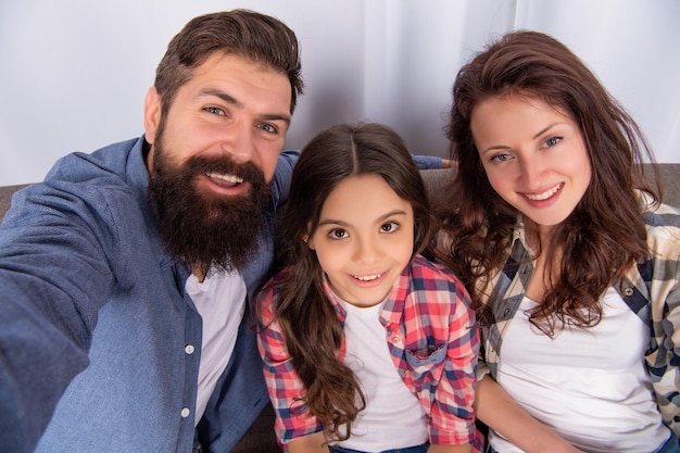 Pais felizes com criança fazendo selfie juntos em casa, dia da família