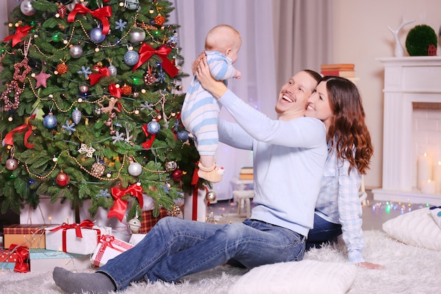 Foto pais felizes com um bebê perto da árvore de natal no chão da sala decorada