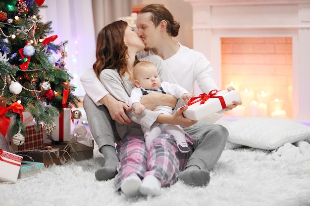 Pais felizes com um bebê perto da árvore de Natal no chão da sala decorada