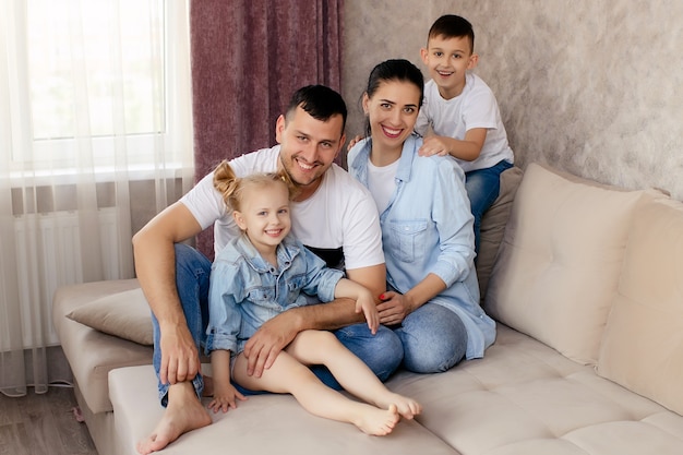 Pais felizes conversando com os filhos em casa, sentados no sofá da sala juntos e sorrindo