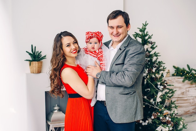 Pais felizes e bebê pequeno em roupas elegantes juntos na sala de natal decorada.