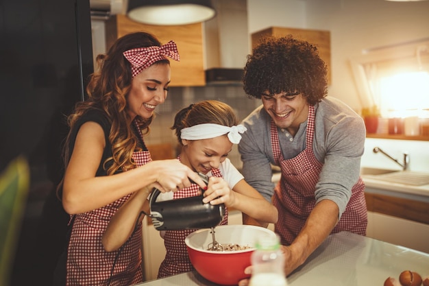 Foto pais felizes e sua filha estão preparando biscoitos juntos na cozinha. a garotinha ajuda os pais a misturar a massa com a batedeira.