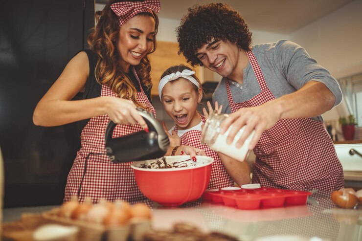 Foto pais felizes e sua filha estão preparando biscoitos juntos na cozinha. a garotinha ajuda os pais a misturar a massa com a batedeira.