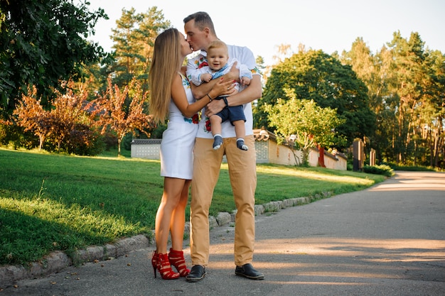 Pais felizes, segurando nas mãos um menino vestido de bordado e beijando