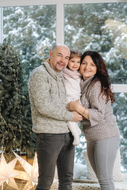 Pais formandos abraçam a neta perto de um pinheiro em casa clima de natal de pessoas felizes