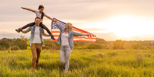 Pais jovens com sua filha segurando a bandeira americana na zona rural ao pôr do sol. Comemoração do Dia da Independência.