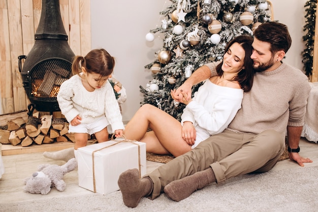 Pais jovens com uma filha pequena perto da árvore de Natal