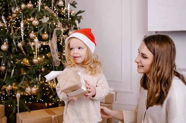 Pais jovens sorridentes dando pequena filha engraçada presente no natal, garota rindo com chapéu de papai noel segurando a caixa nas mãos. feriado familiar. feriados, presentes, natal, conceito de natal