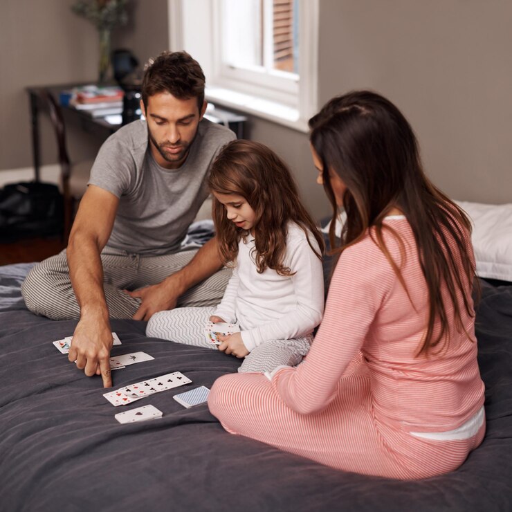 Foto pais menina e jogar cartas para relaxar para se divertir com ligação aprendizagem e jogos com estratégia no quarto de casa pai mãe e filha na cama matemática e ensino com conexão na casa da família