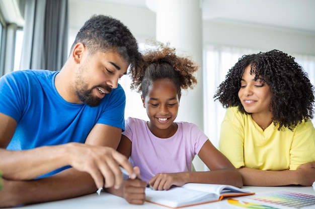 Pais multiétnicos ajudando a filha com a lição de casa em casa Jovem pai e mãe ajudando a filha a estudar na sala de estar Menina completando seus exercícios com a ajuda do pai e da mãe