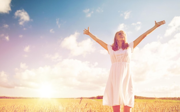 país, naturaleza, vacaciones de verano, vacaciones y concepto de la gente - joven sonriente vestida de blanco en el campo de cereal