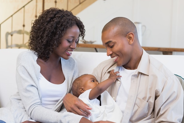 Pais novos felizes que passam o tempo com o bebê no sofá em casa na sala de estar