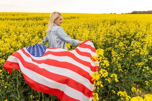 país, patriotismo, día de la independencia y concepto de la gente - mujer joven sonriente feliz con la bandera nacional americana en el campo.