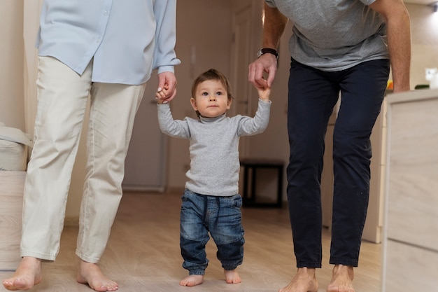 Foto pais segurando as mãos do filho para sua vista frontal dos primeiros passos