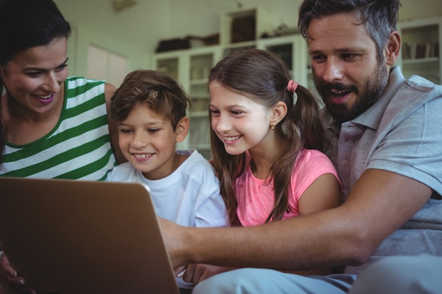 Pais sentados no sofá com seus filhos e usando o laptop na sala de estar