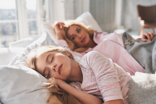 En el país de los sueños. Hermosa joven madre mirando a su linda hija deslizante y sonriendo mientras está acostado en la cama en casa