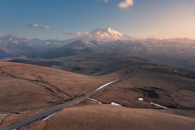 Paisagem aérea com estrada ao longo das colinas até a montanha alta coberta de neve MtElbrus Rússia