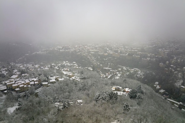 Paisagem aérea nebulosa com penhascos de montanha cobertos de neve recém-caída durante fortes nevascas na floresta de montanha de inverno em um dia frio e tranquilo