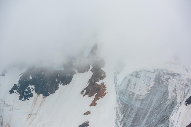 Paisagem alpina atmosférica com geleira na parede da montanha de neve em densas nuvens baixas Paisagem montanhosa impressionante com geleira nas rochas em nuvens baixas e espessas Alta montanha de neve com geleira de gelo no nevoeiro