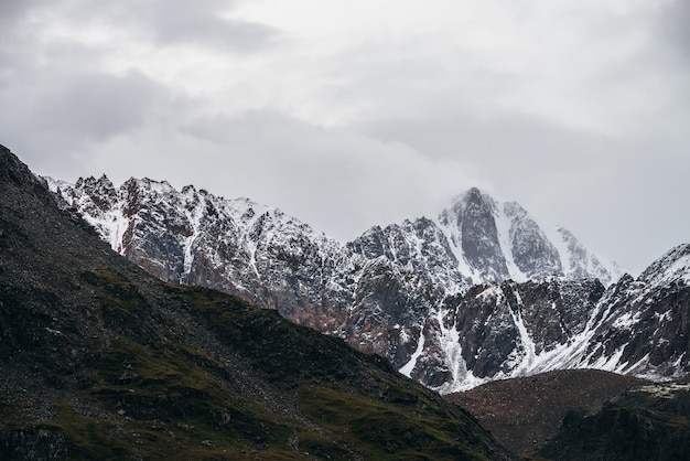 Paisagem alpina atmosférica com grande pico de montanha com neve em nuvens baixas. Paisagem montanhosa dramática com pináculo em tempo nublado. Vista incrível para o pico nevado pontudo em céu nublado.