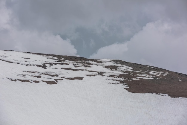 Paisagem alpina atmosférica com parede de montanha de neve alta sob nuvens chuvosas no céu cinza Cenário nublado dramático com grande topo de montanha de neve sob céu nublado cinza Tempo sombrio em alta altitude