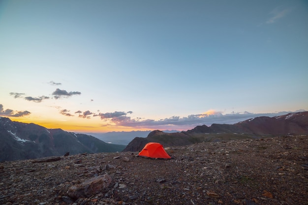 Paisagem alpina cênica com tenda em altitude muito alta com vista para grandes montanhas no céu laranja do amanhecer Tenda laranja vívida com vista incrível para a cordilheira alta sob céu nublado nas cores do pôr do sol