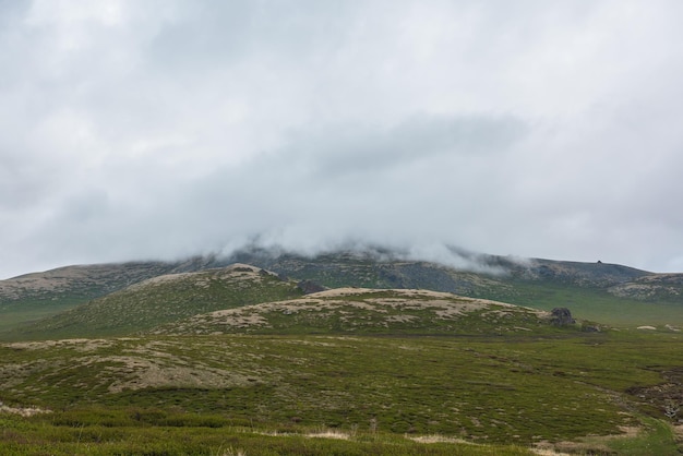 Paisagem alpina dramática com colinas e montanhas em nuvens baixas cinzentas Cenário atmosférico sombrio da tundra sob o céu cinza chumbo Vista minimalista sombria para colinas verdes entre nuvens chuvosas baixas em nublado